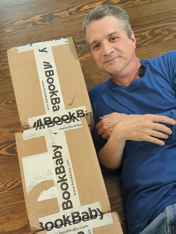 Matthew Delbert Gillmore lying beside a shipment of new books from BookBaby printer.